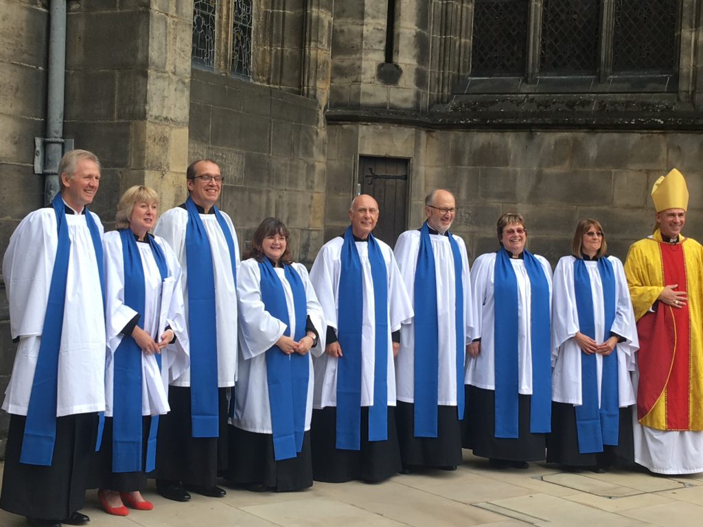 A group of lay readers wearing blue lay reader vestments gathered for a photo outside a cathedral.