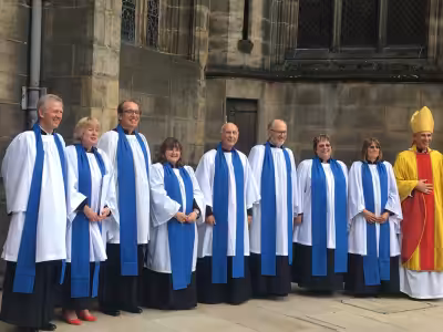 A group of lay readers wearing blue lay reader vestments gathered for a photo outside a cathedral.