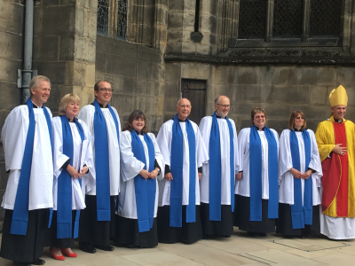 A group of lay readers wearing blue lay reader vestments gathered for a photo outside a cathedral.