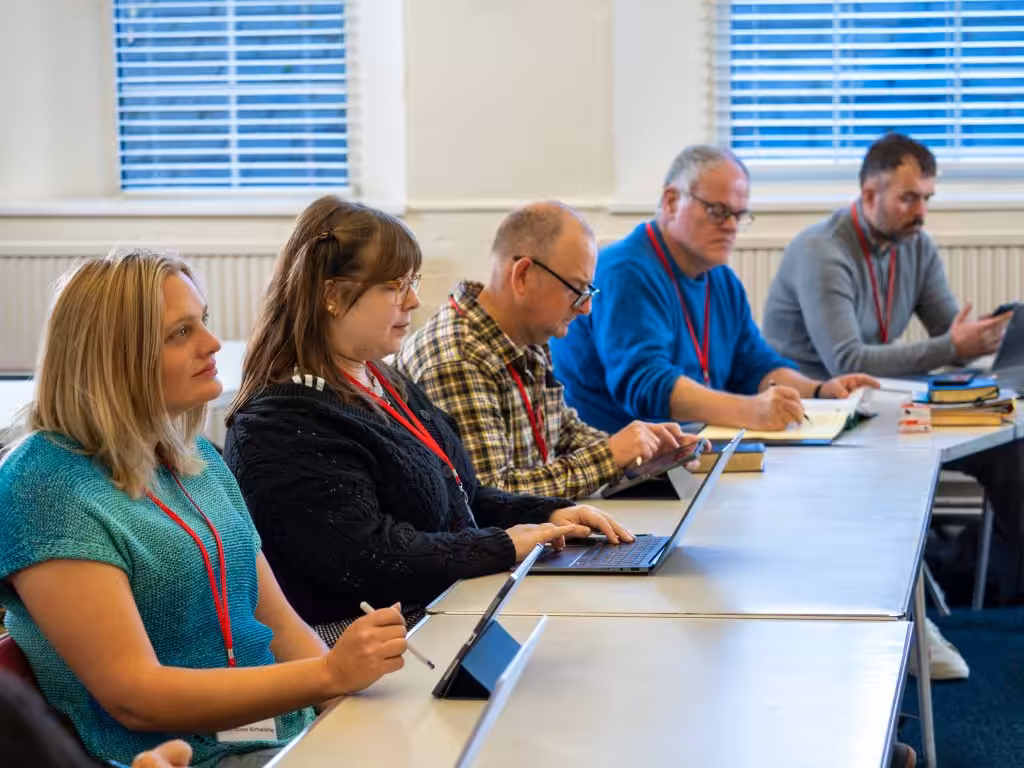 People of all ages sitting at desks in a classroom with laptops looking very studious