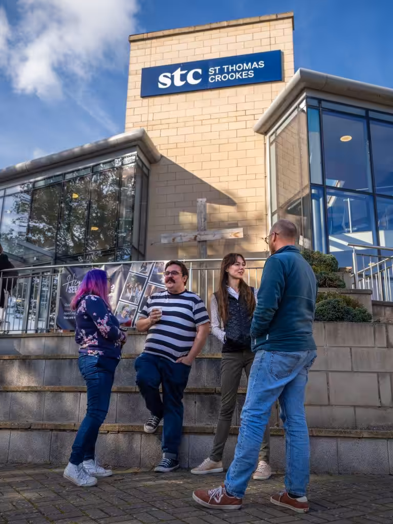 Young people talking and socialising outside a building made of pale bricks and glass panels