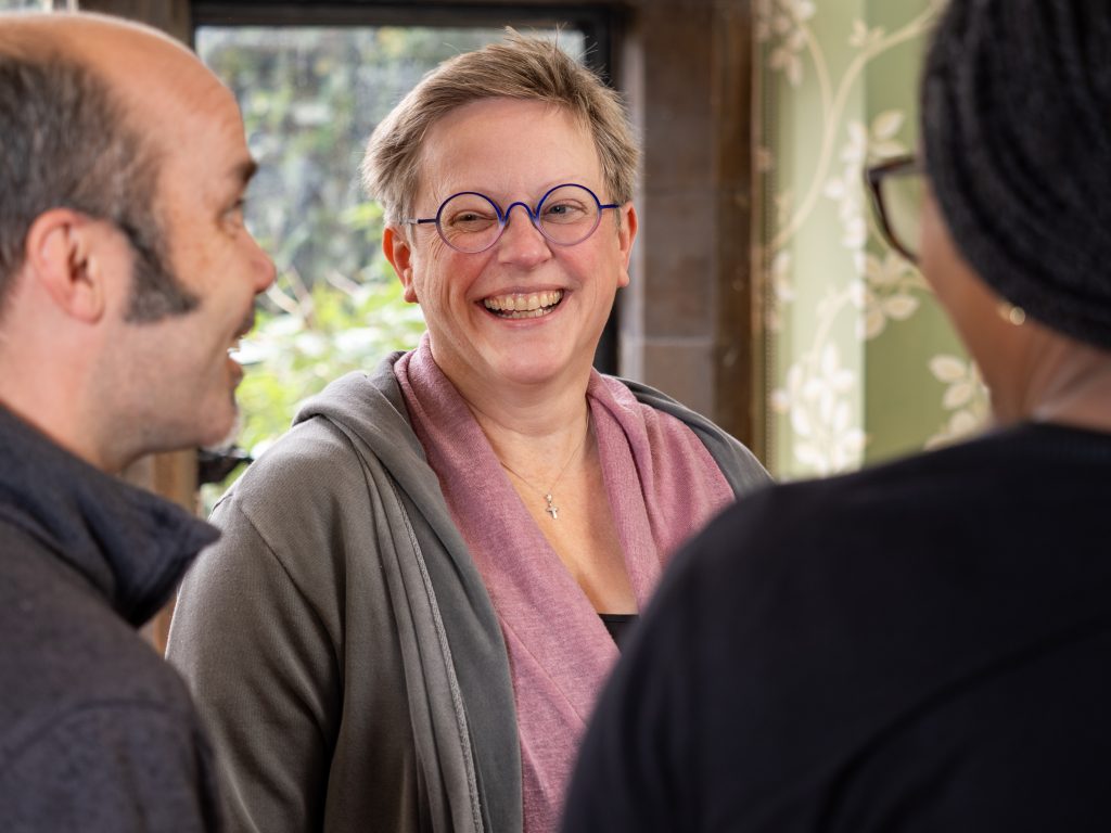Three people laughing and talking in a room with green wallpaper